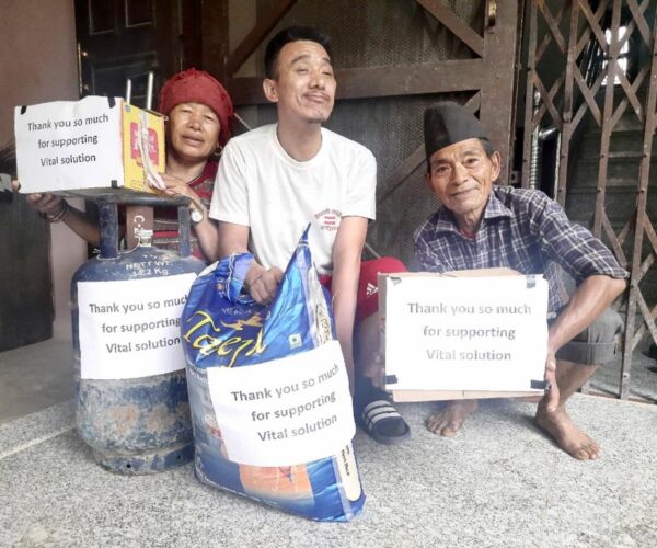 Vital Solutions Work in Nepal, three individuals holding Vital Solutions donations and signs, outdoors.