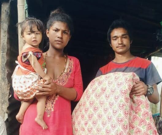 Vital Solutions Work in Nepal, young parents holding toddler and blanket in Nepal, in doorway.